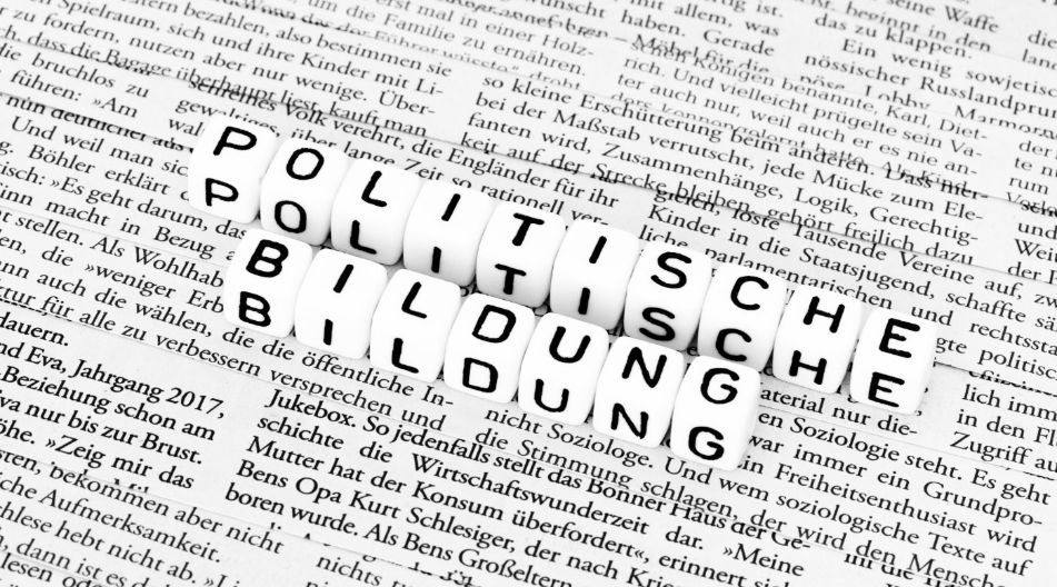 Buchstabenwürfel bilden die Worte "POLITISCHE BILDUNG" und liegen auf einer Zeitungsseite mit schwarzem gedrucktem Text. Buchstabenwürfel bilden die Worte "POLITISCHE BILDUNG" und liegen auf einer Zeitungsseite mit schwarzem gedrucktem Text.